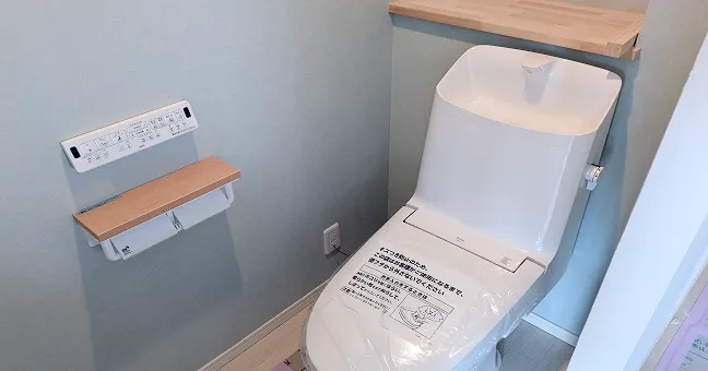 グレーのクロスに木製棚が映える、落ち着いた雰囲気のトイレ空間