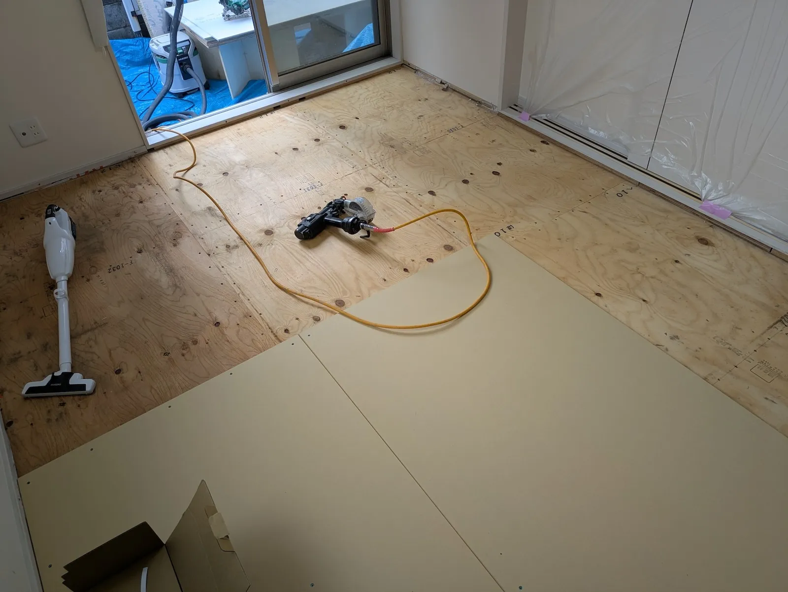 構造用合板の下地にフロアタッカーで床材を張る施工中の様子