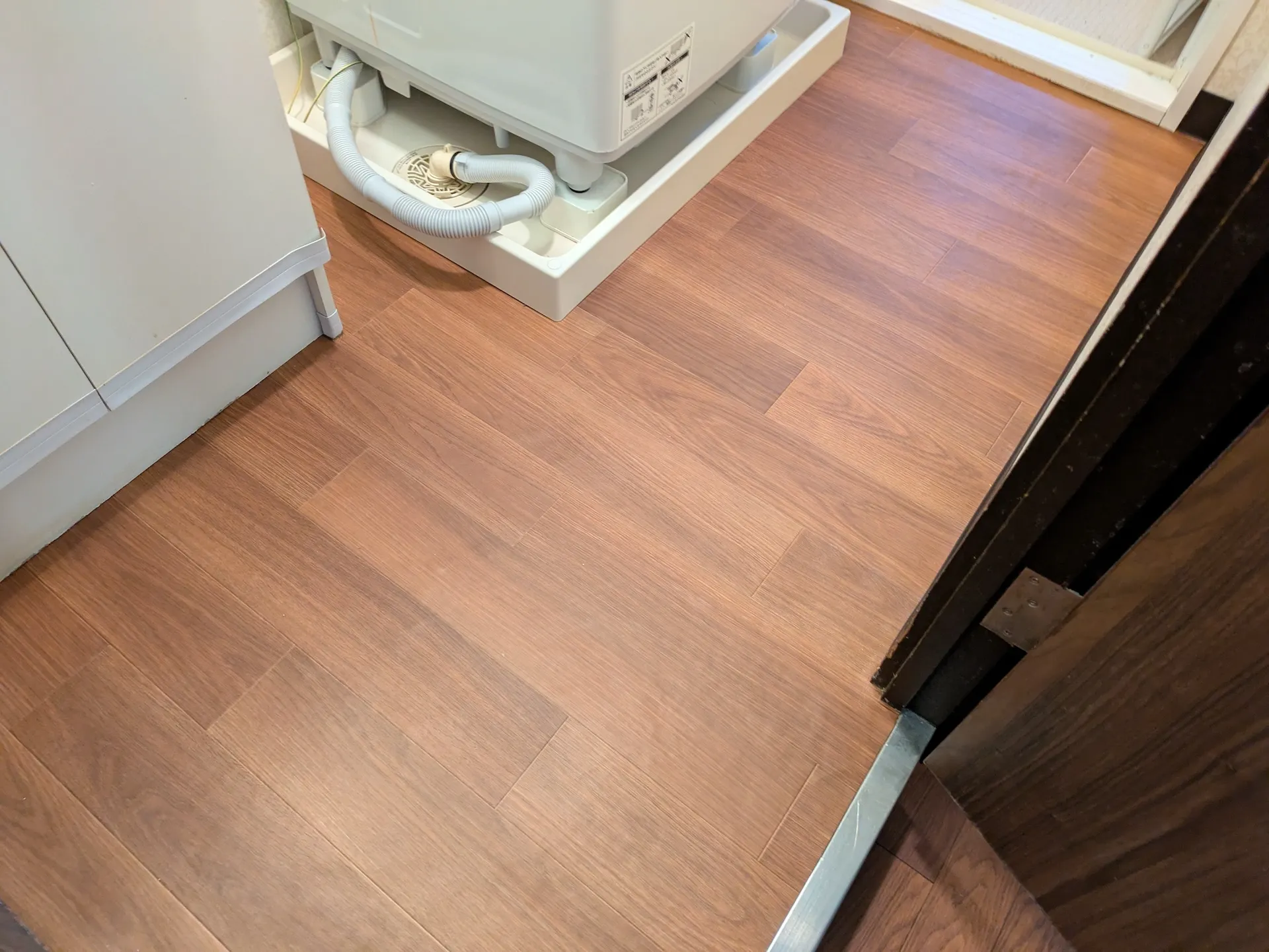 洗面脱衣所の洗濯機パンと新しく張り替えられた木目調のフローリング