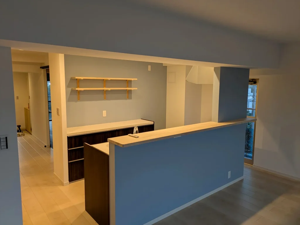 機能美を追求したカウンターキッチンのリノベーション。ブルーの壁紙と造作棚のあるモダンな空間