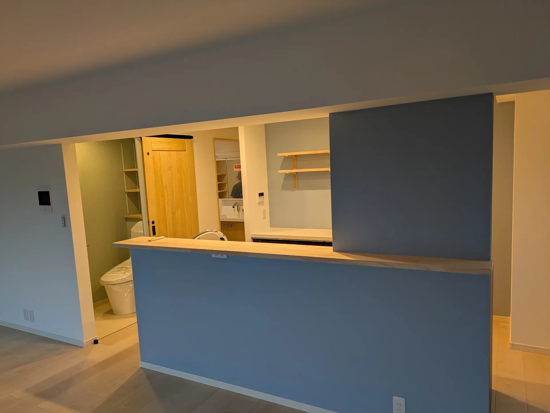 機能美を追求した、ブルーの壁紙が映えるカウンターキッチンのリノベーション。奥に洗面台・トイレのあるモダンな空間。