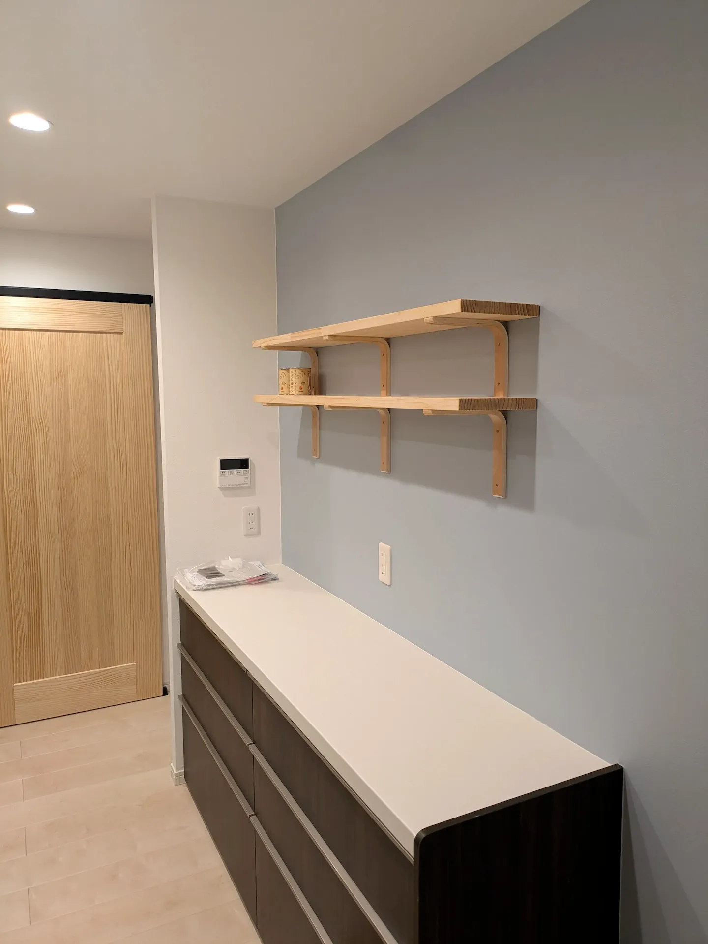 北欧風のブルーグレーの壁紙と木製ウォールシェルフのあるキッチン背面