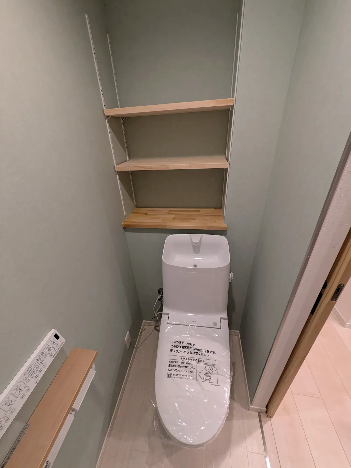 グレーのクロスに木製棚が映える、落ち着いた雰囲気のトイレ空間