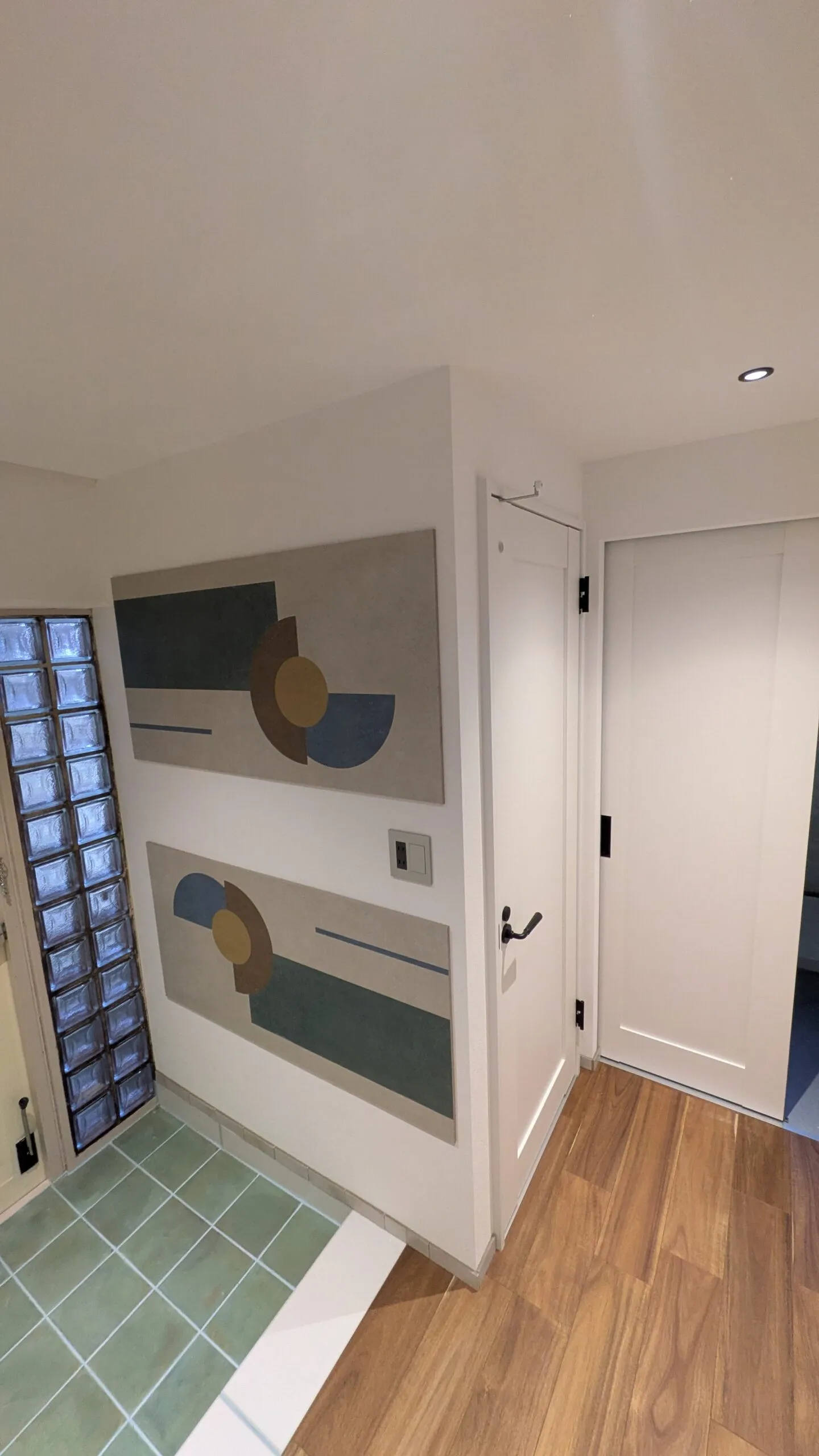 採光用のガラスブロックと塗り壁に飾られた現代アートのあるおしゃれな玄関