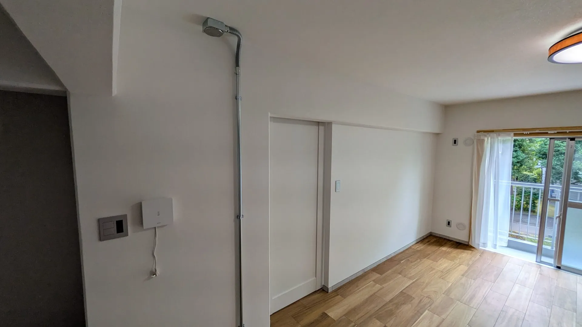 白壁に映える金属製の露出配管とシンプルな白い引き戸