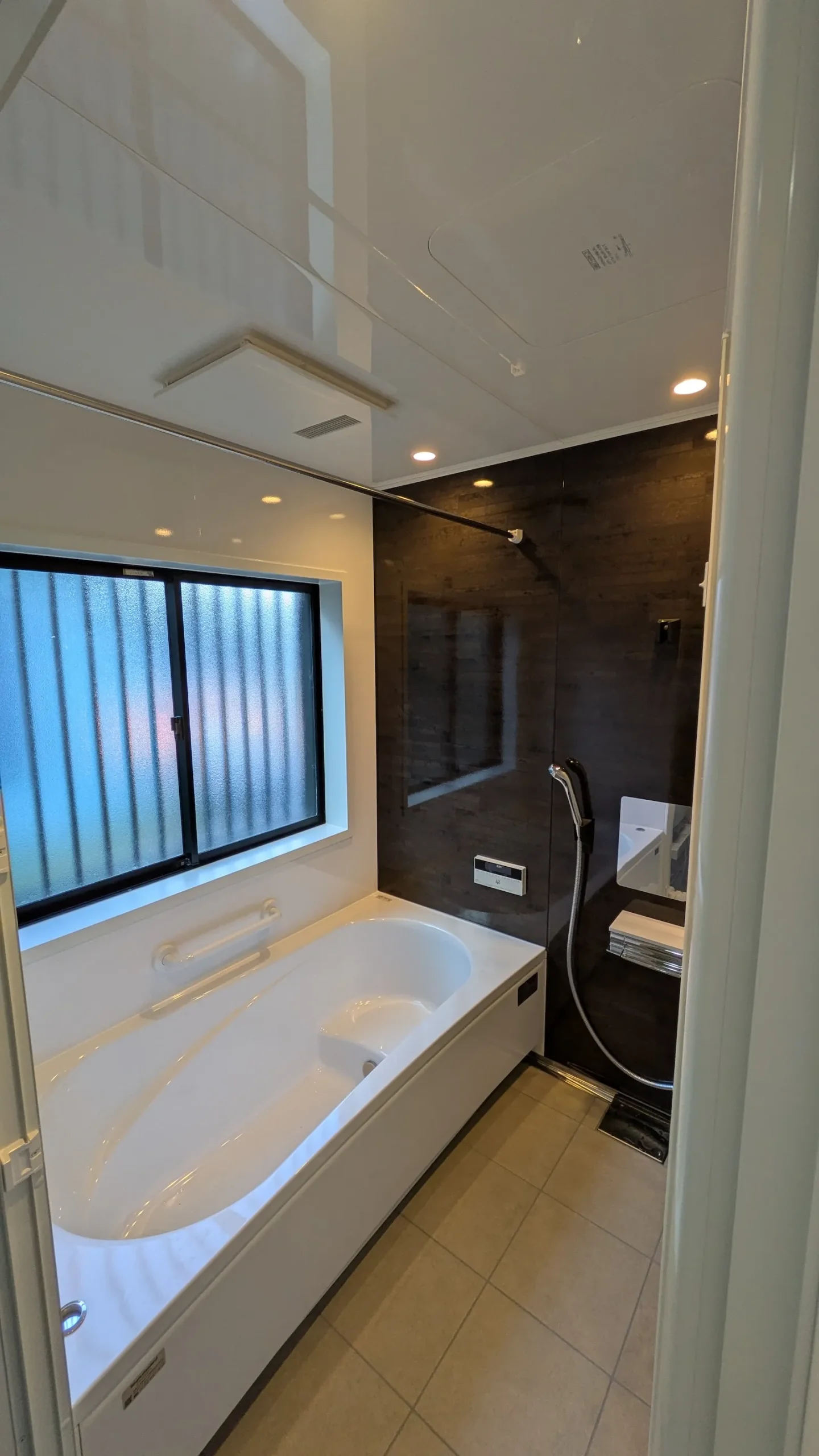 ダークブラウンのアクセントパネルが映えるモダンな広々とした新しい浴室