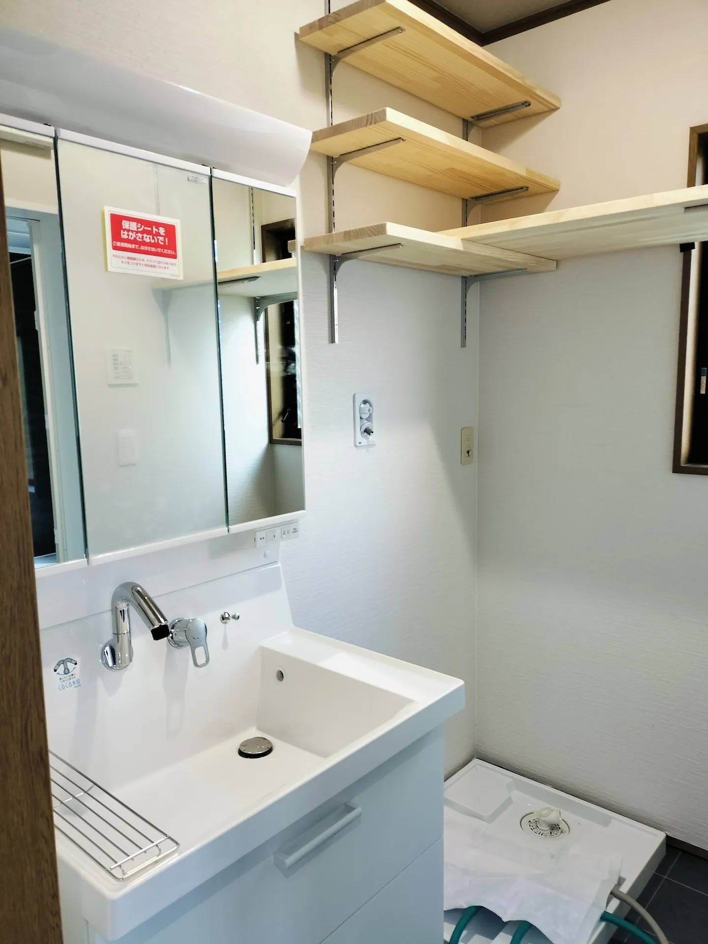 清潔感のある新しい洗面化粧台とその上の空間を活用した木製棚